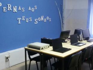 Sala com computadores. Numa parede amarela lê-se "(d)á pernas aos teus sonhos"