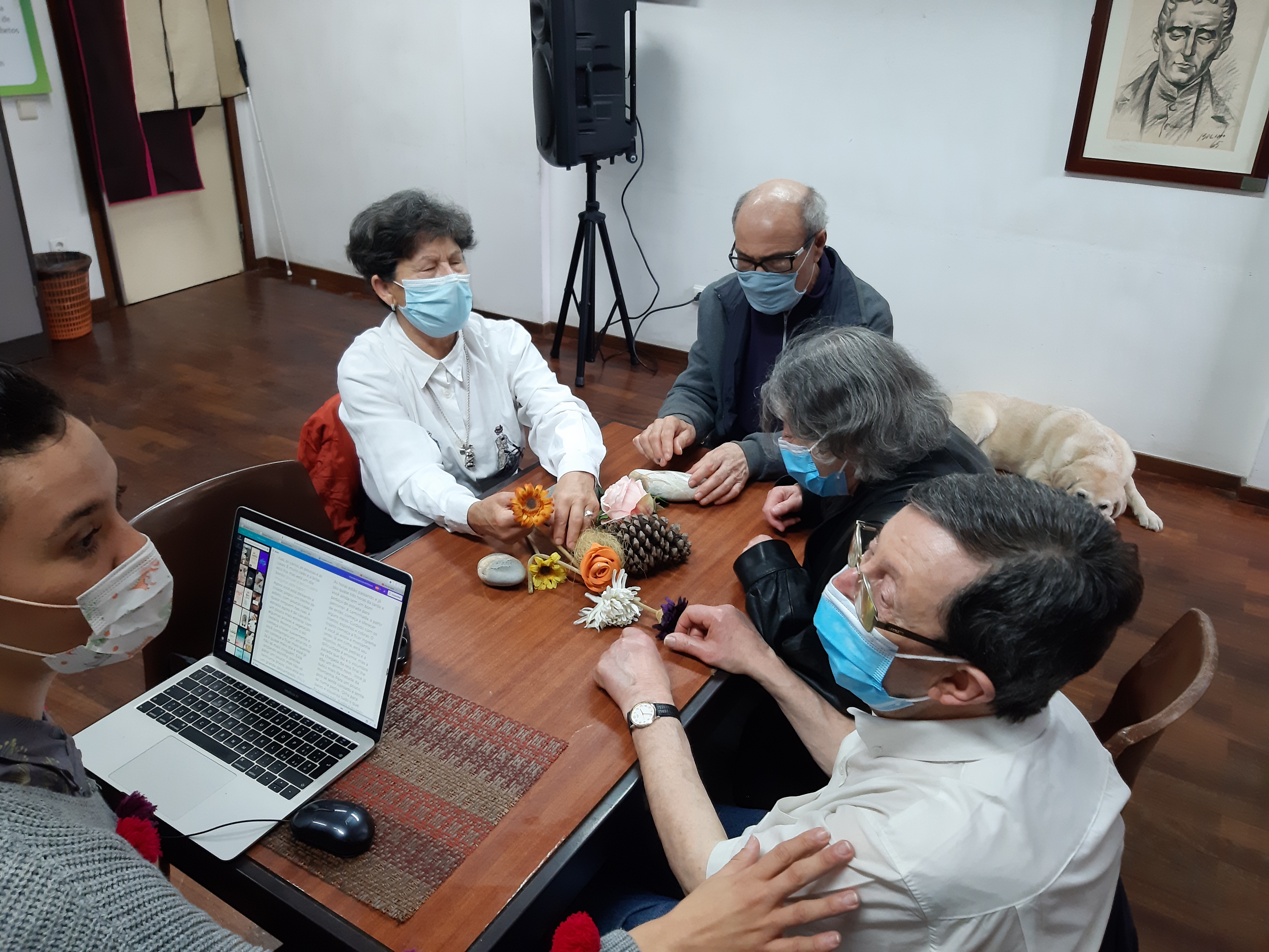Fotografia tirada durante a atividade onde se vê o grupo de participantes a tatear alguns elementos da natureza: flores, pedras e pinhas