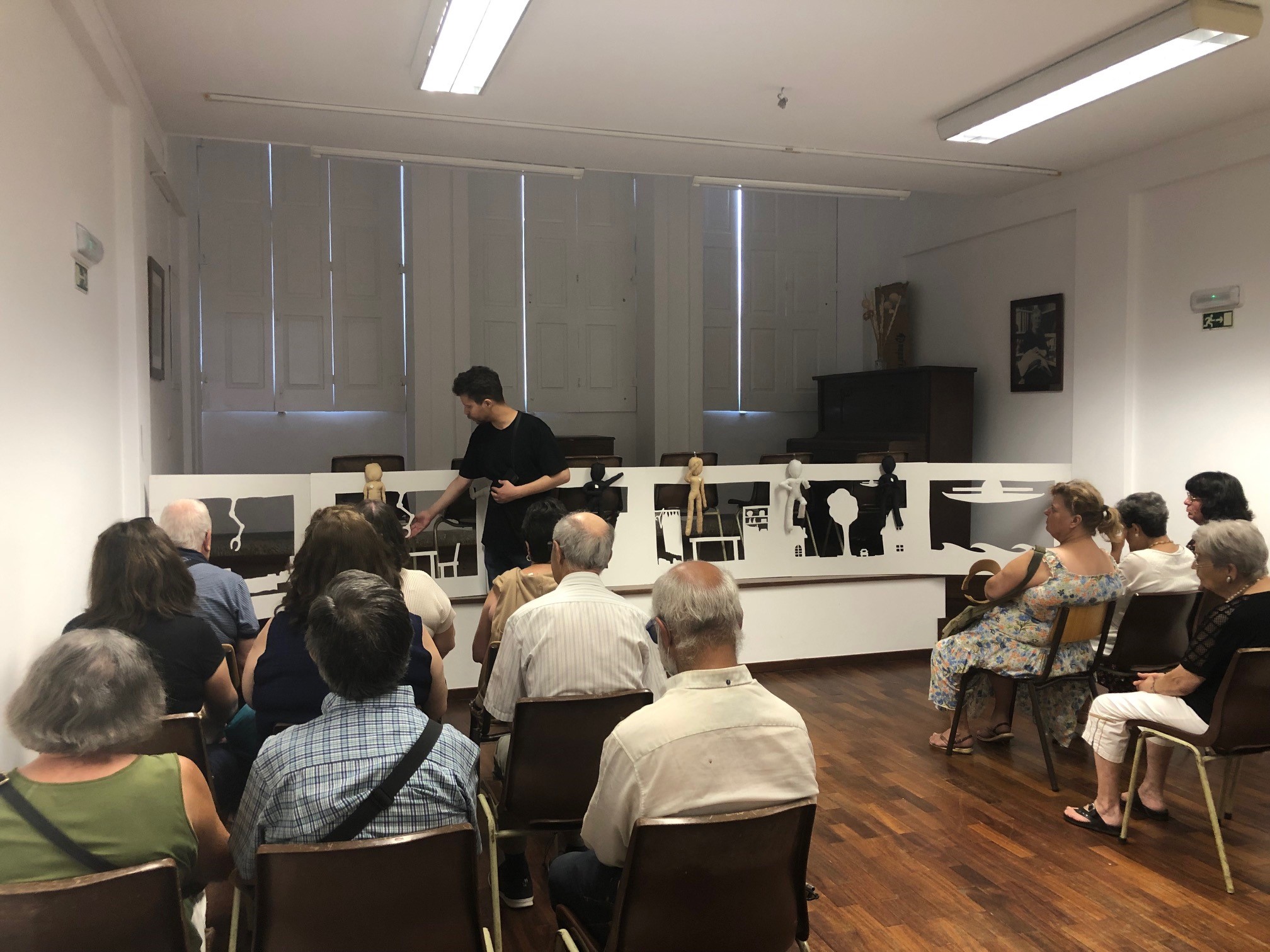 Peça de Teatro JCH plano geral da sala onde decorreu a peça. De costa, vemos o público sentado e, de frente, o palco com os 6 cartões do cenário e o ator