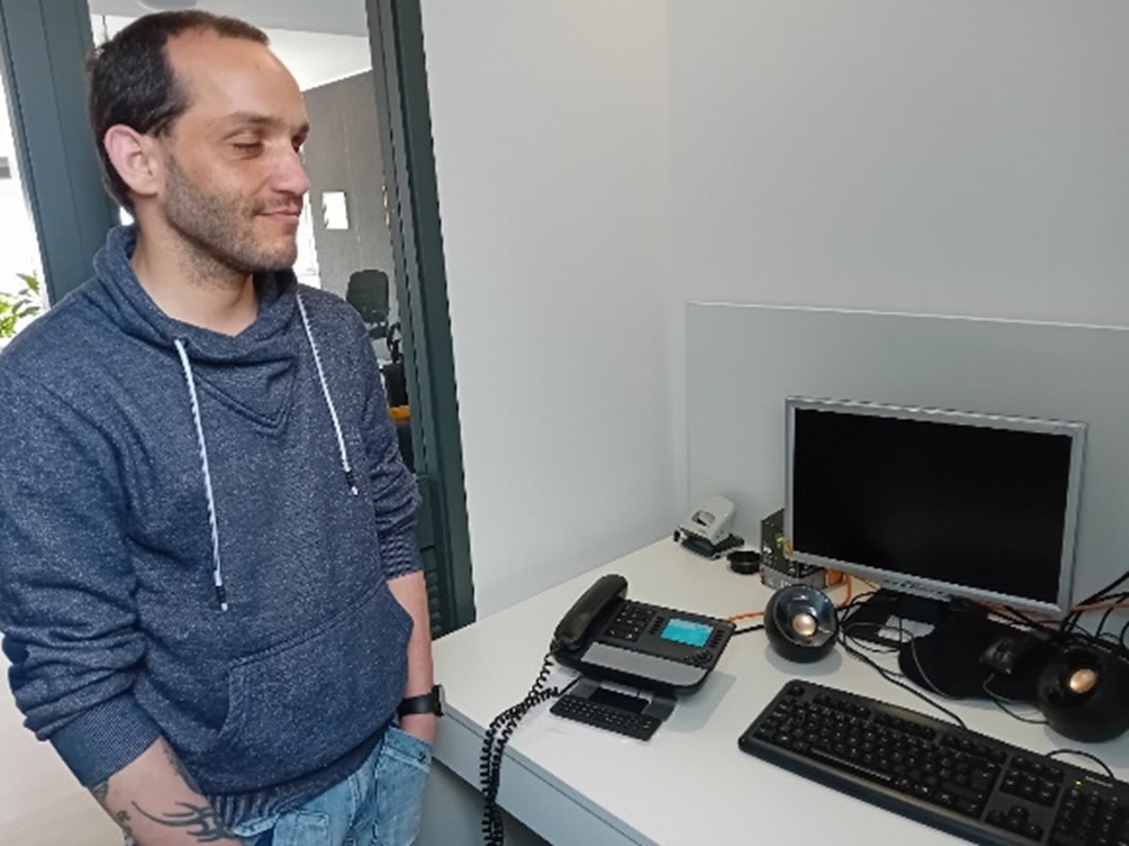 Rafael Simões pousa para a foto no seu posto de trabalho. Na foto vê-se um computador e um telefone fixo.