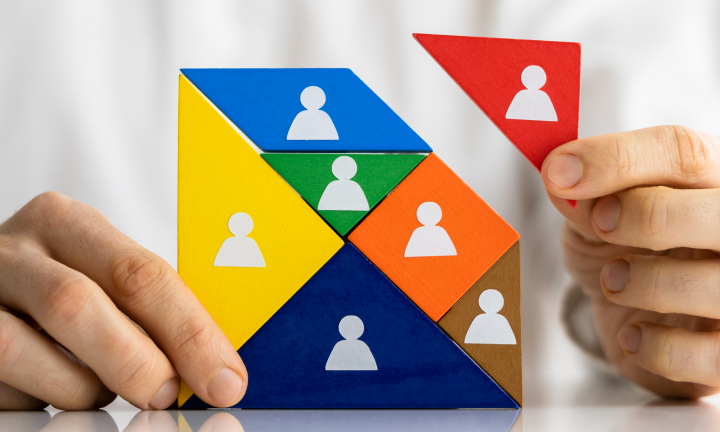 Imagem de duas mãos a completarem um tangram, onde cada peça tem uma cor e o desenho de um ícone de uma pessoa.