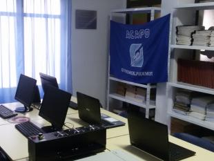 Sala com computadores. Do lado direito, uma parede com livros Braille e uma bandeira com logótipo ACAPO e mensagem "Queremos podemos"