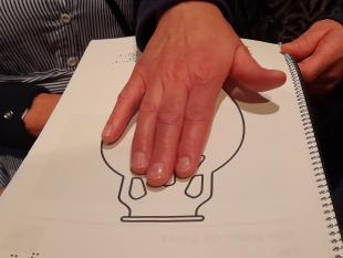 Mão de uma participante a tatear um dos materiais do kit de informação multiformato, que inclui informação em Braille sobre as peças em exposição no museu.