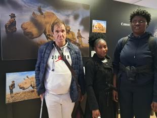 3 visitantes, 1 homem e 2 mulheres, junto à fotografia "Guerras de Rinocerontes" por Brent Stirton 