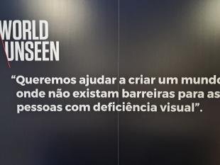  Placard preto onde está escrito, a branco, World Unseen “Queremos ajudar a criar um mundo onde não existam barreiras para as pessoas com deficiência visual”.