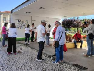 Várias pessoas, algumas delas com deficiência visual, reunidas em conversa no jardim, junto ao mural.  