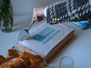 Fotografia zoom onde é possível ver-se a mão da Diretora Técnica da Delegação, Carina Ferreira, enquanto corta o bolo de inauguração que contém o logotipo da ACAPO