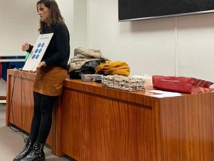 Vânia Vieira, Técnica de Orientação e Mobilidade, durante a explicação sobre a célula Braille. Na mãos segura uma cartolina A3 onde está impressa a célula Braille.
