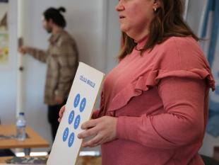 Maria da Luz Ribeiro com um cartaz nas mãos onde se vê a célula Braille impressa.