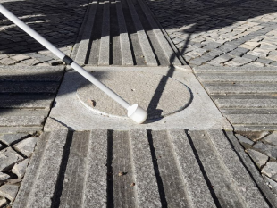Bengala branca que contorna a placa quadrada de granito, com um círculo em relevo no interior, simulando uma "rotunda", num cruzamento de linhas-guia