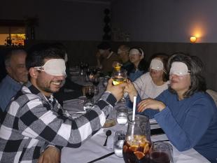 Participantes no jantar às escuras, de olhos vendados, fazem um brinde.