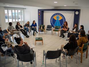 Sentados em cadeiras, colocadas de modo a formar um grande círculo, os participantes partilham as suas vivências e experiências numa das salas da Fundação Lar de Cegos. Por trás deles é possível ver-se uma lona grande com o logotipo da instituição.