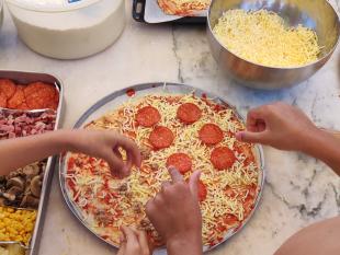 Mesa onde as crianças estão a preparar as pizzas para o almoço e onde é possível ver-se os diversos ingredientes disponíveis 