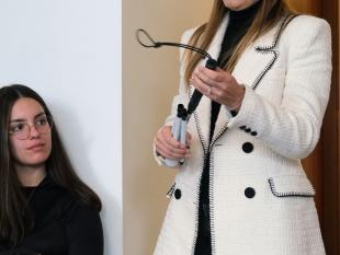 Fotografia tirada durante o workshop onde é possível ver-se a Técnica de Orientação e Mobilidade, Inês Ferreira, de pé, com uma bengala dobrada na mão enquanto fala com os participantes.