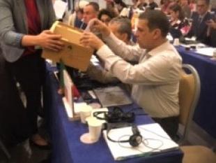 Rodrigo Santos coloca o boletim de voto na urna de voto que é segurada por uma mulher. 