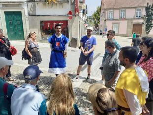 O grupo, o guia, o tradutor audiovisual e os voluntários em roda, a escutar o guia enquanto este explica a contextualização história da Viagem Medieval e do local onde se encontram. 