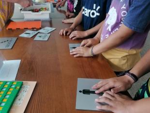 Fotografia onde é possível ver-se as crianças que participaram nesta ação a tatear alguns objetos, nomeadamente placas sinaléticas com relevo e peças do LEGO Braille Bricks.