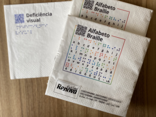 2 embalagens dos Guardanapos Solidários ao lado do guardanapo com a palavra "Deficiência visual"