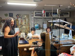 Tânia Gil, em pé, no interior do atelier a falar para as participantes, que se encontram sentadas.