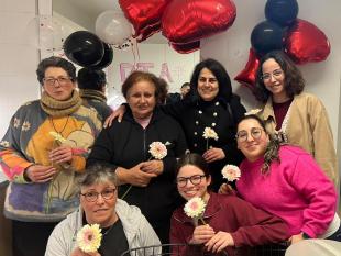 Grupo de mulheres que participaram na atividade pousa sorridente para a foto junto do espelho e dos balões. Cada uma segura na mão a sua gerbera.
