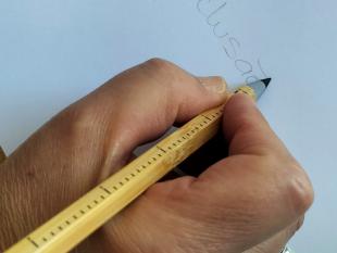 Uma senhora escreve a palavra inclusão numa folha utilizando o lápis infinito 3 funções da ACAPO.