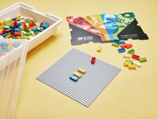 Fotografia onde é possível ver a caixa, as bases e as peças do kit LEGO® Braille Bricks.