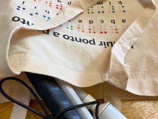 Tote Bag Alfabeto Braille em cima de uma mesa vendo-se no seu interior uma bengala branca dobrada.