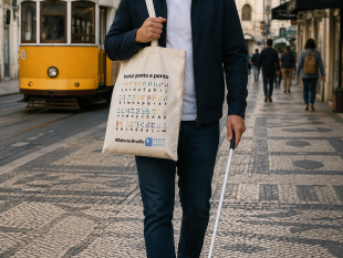 Rapaz cego a andar numa rua de Lisboa utilizando o tote bag. Na imagem vê-se o elétrico 28.