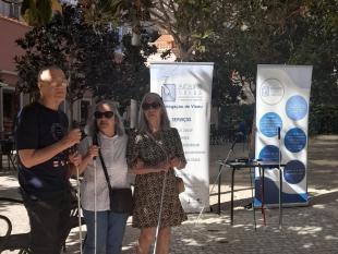 Três Associados perto de uma mesa onde estão colocadas algumas bengalas brancas. Ao lado da mesa estão dois roll up com o logotipo da ACAPO, a missão e os serviços que disponibiliza.